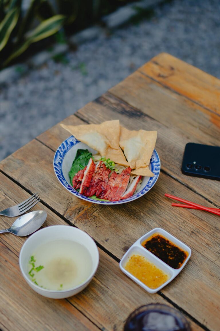 A delicious Asian dish with soup and sauces served outdoors on a rustic wooden table.