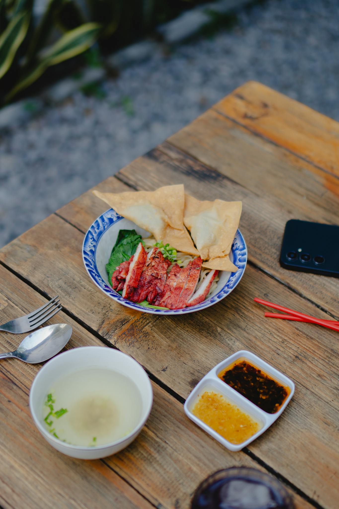 A delicious Asian dish with soup and sauces served outdoors on a rustic wooden table.