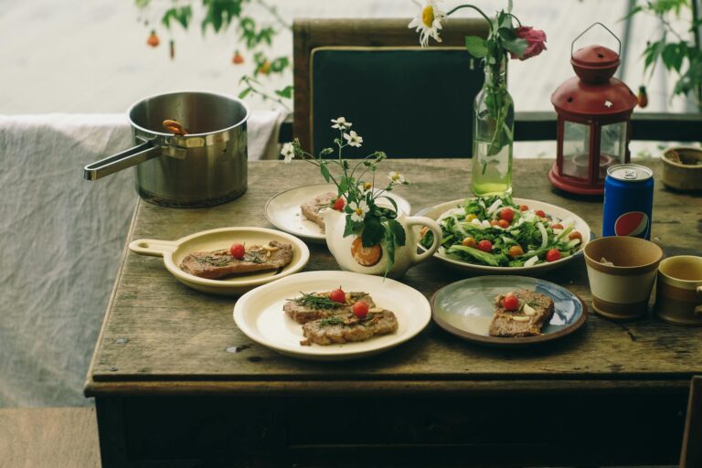 A rustic dining table adorned with meat dishes, fresh salad, and vintage decor, creating a cozy outdoor meal setting.